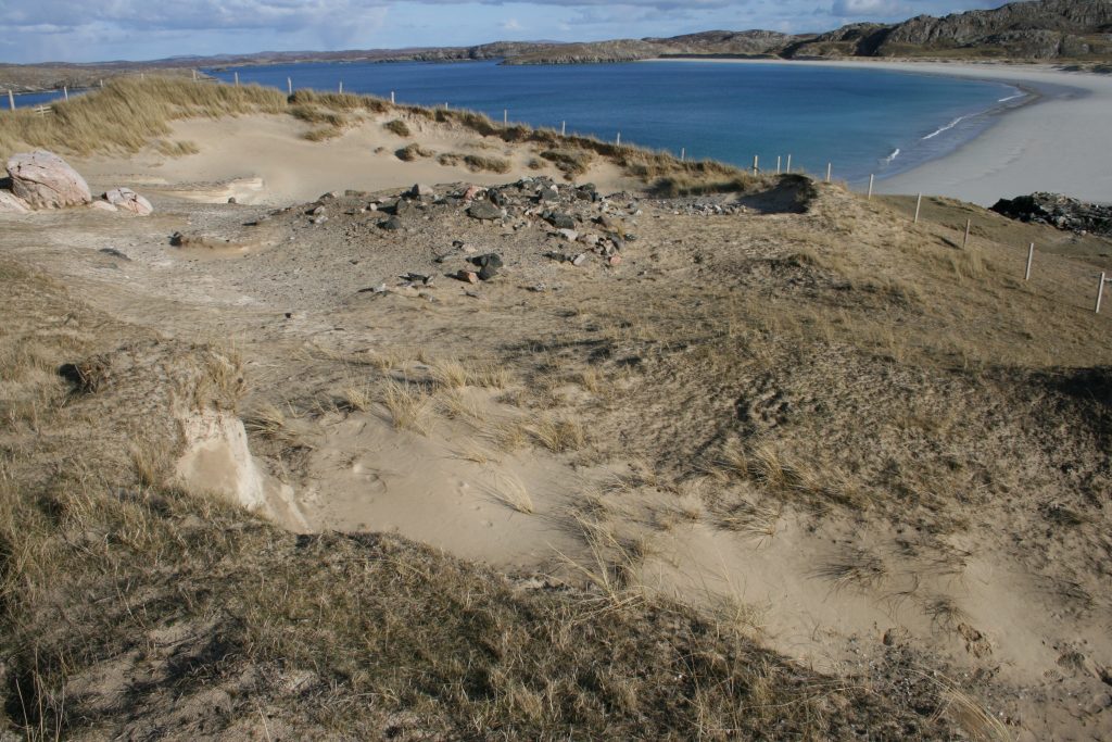 An exposed area of sand above a beach, with a damaged cairn