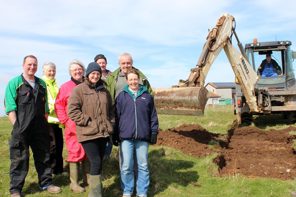 The first cut. Members of the Sanday Development Trust and the Community Council oversee the evaluation of the proposed site of the re-located Meur burnt mound.