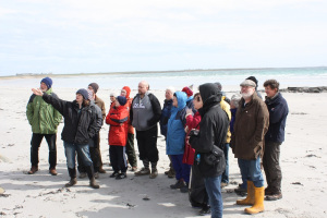 A group of people standing on a beach as one person talks and points