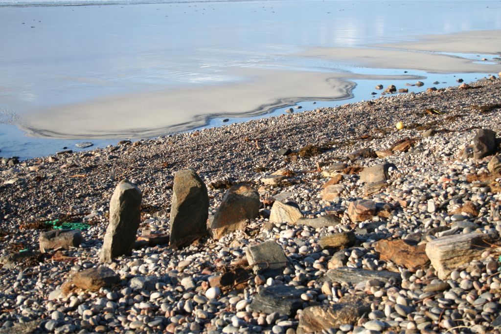 Large upright stone slabs standing in a line on a pebble beach