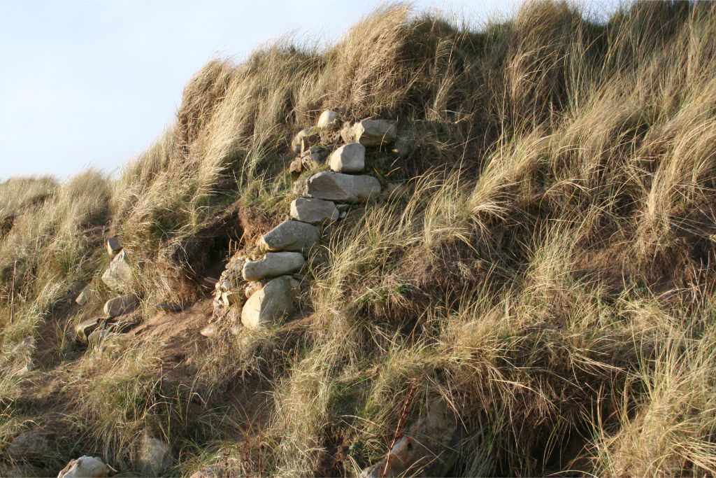 A sand dune with the end of a stone wall protruding from the face