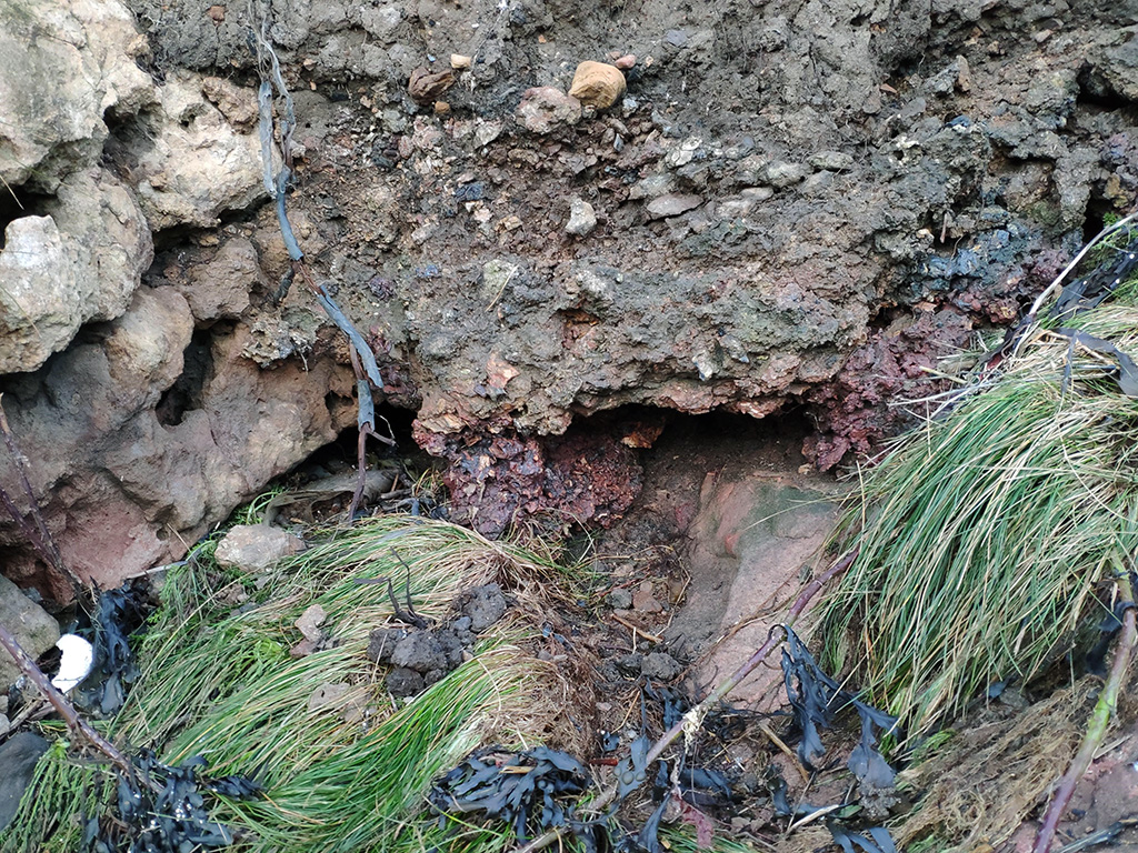 Cross section of reddish fuel slag filling a channel in the coast edge