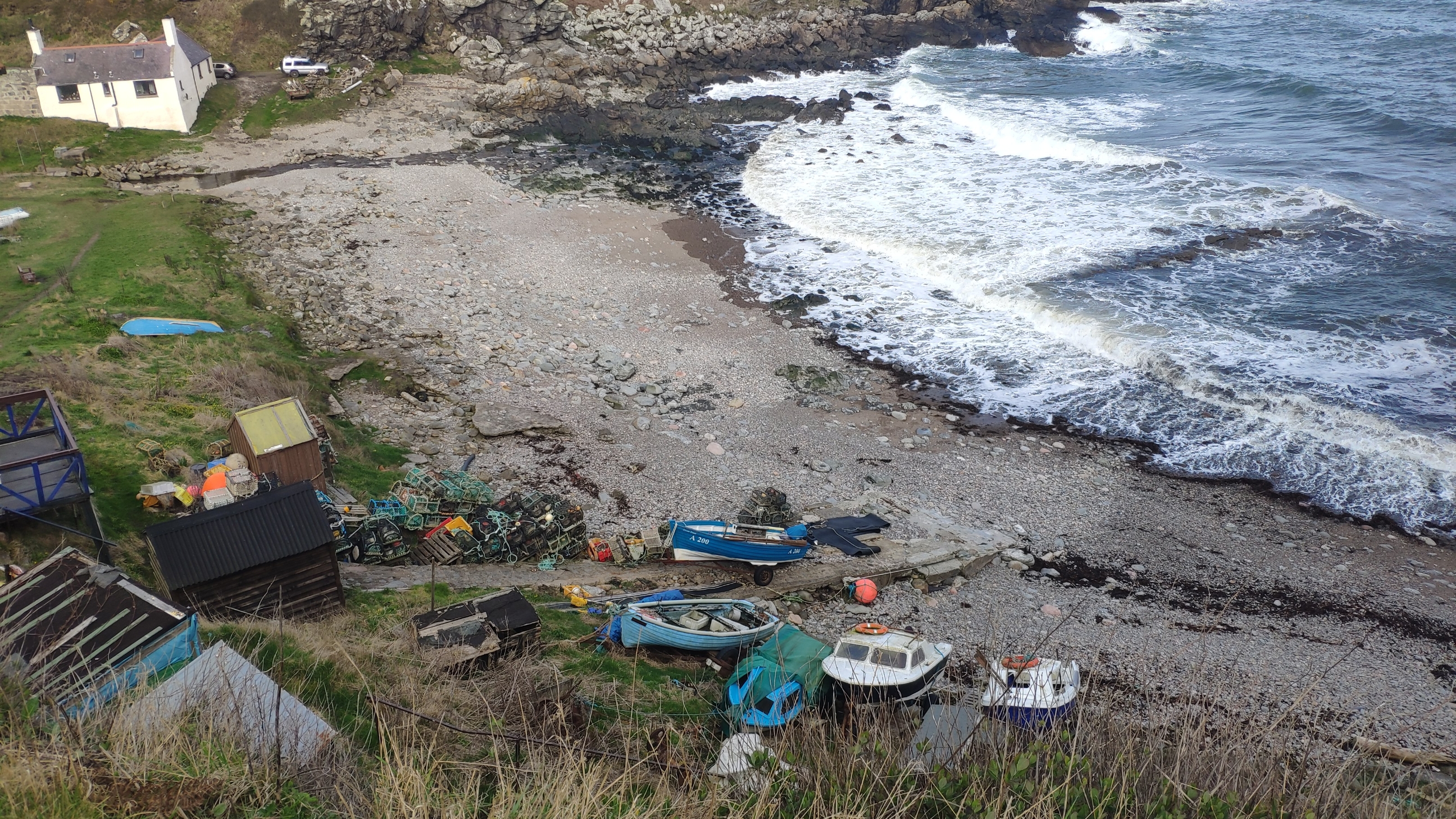 General view of harbour. Old pier visible partially submerged in the middle of the bay. Railed slipway in background in front of the landrover. Current slipway in foreground.