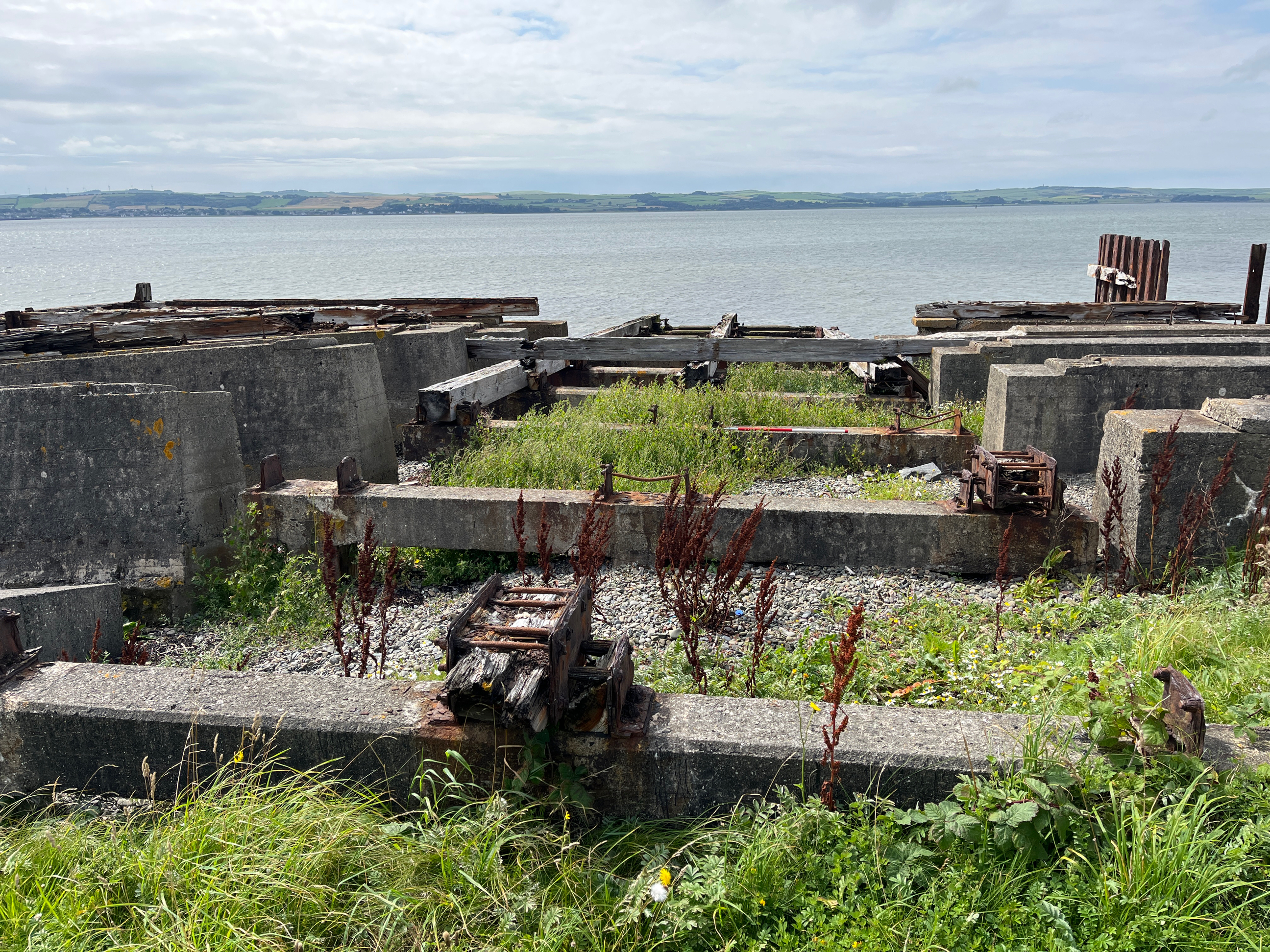 Concrete remains of slipway with corroded iron fixings. Some wooden sections still visible within cast iron. 